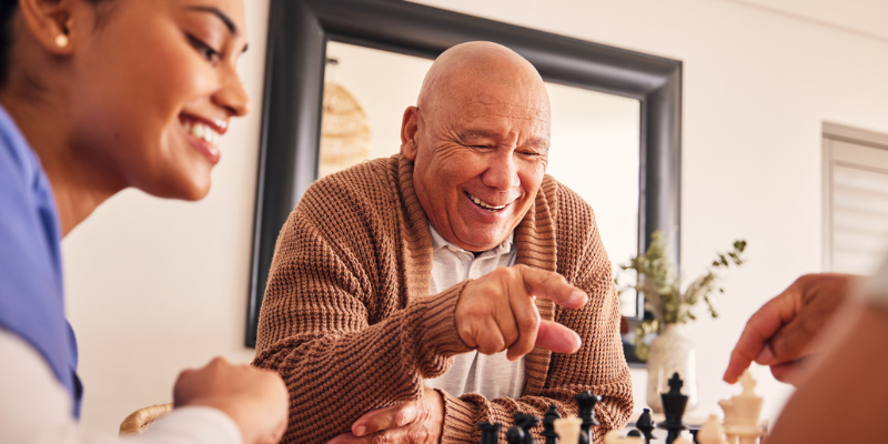 personal care vs. companion care illustration with a caregiver playing chess with senior